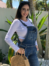 Load image into Gallery viewer, Blue denim overalls with rip on the right knee and rips at the bottom cuffs. 