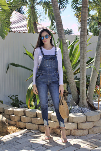 Blue denim overalls with rip on the right knee and rips at the bottom cuffs. 